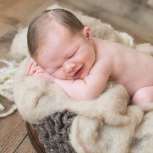 Smiling newborn boy in bucket with chunky brown blanket and wool