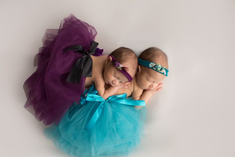Newborn twin girls posed on top of one another white with teal and purple tutus and headties Gainesville Florida photos shoot from above