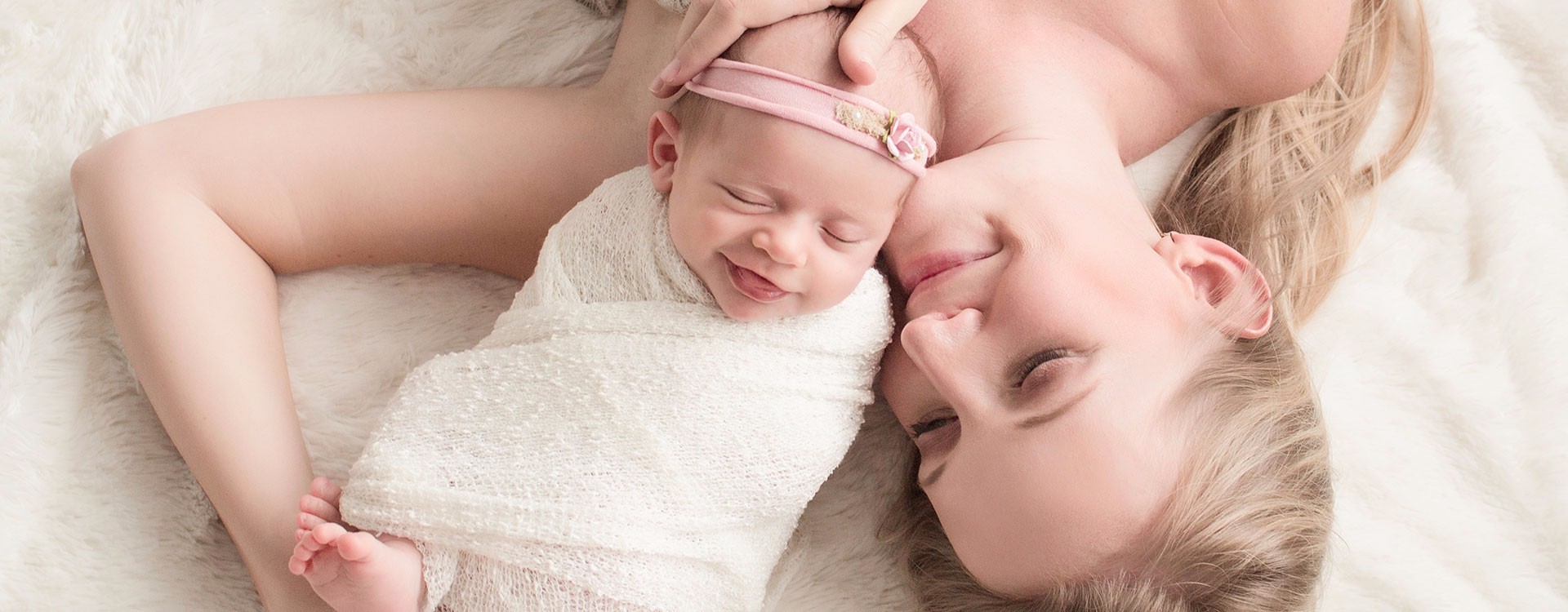 Mom wrapped in champaign lace cuddling Newborn girl Isla wrapped in white with pink floral headband on white fur blanket photo taken from above photos Gainesville FLorida