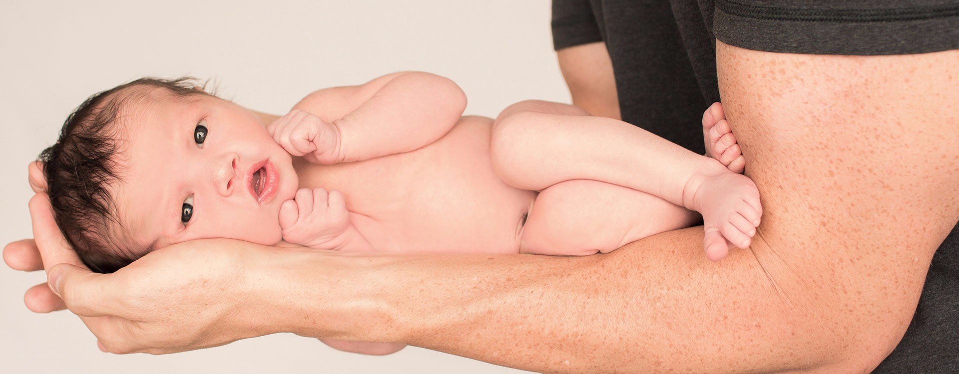 Newborn girl head full of dark hair posed naked on her side along dad's muscular arms Gainesville Florida photo