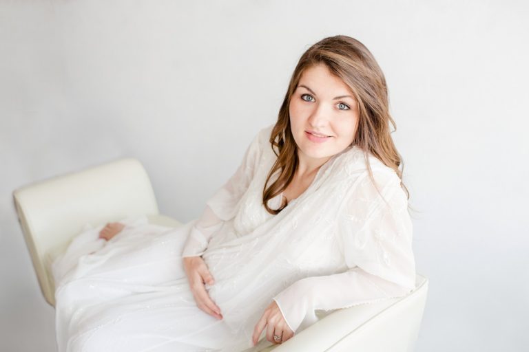 Beautiful pregnant mom holding baby bump lounging on white leather sofa Gainesville Florida maternity photo