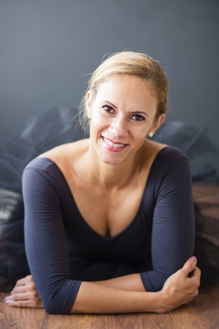 Beautiful woman big brown eyes smiling celebrates beauty with dance posed on wood floor propped on elbows black tutu pink pointe shoes Gainesville Florida Womens Portraiture