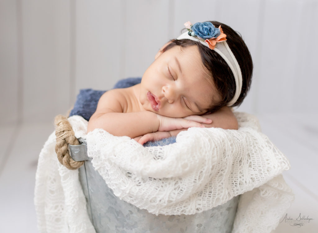 Newborn girl in tin bucket with orange and blue headtie