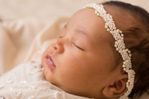 Newborn girl with pearls head tie and flowers on lace