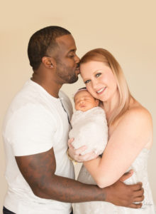 Mother and father with newborn and dad kisses mom