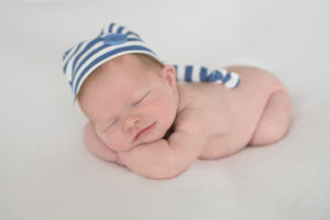 Newborn boy with striped blue hat propped up on arms 