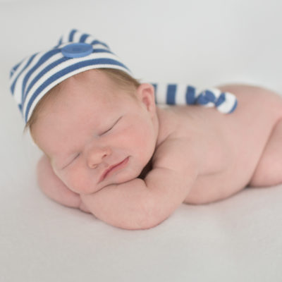 Newborn boy with striped blue hat propped up on his arms