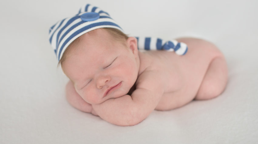 Newborn boy with striped blue hat propped up on his arms