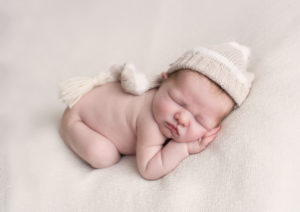 Baby boy with striped cream and beige hat on white blanket