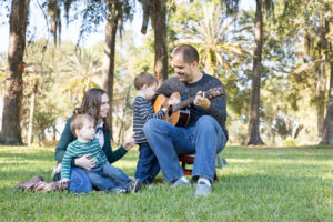 Family photo session at park with two year old twin boys help Dad play guitar
