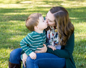 Family photo session at park with two year old twin boy kissing mom