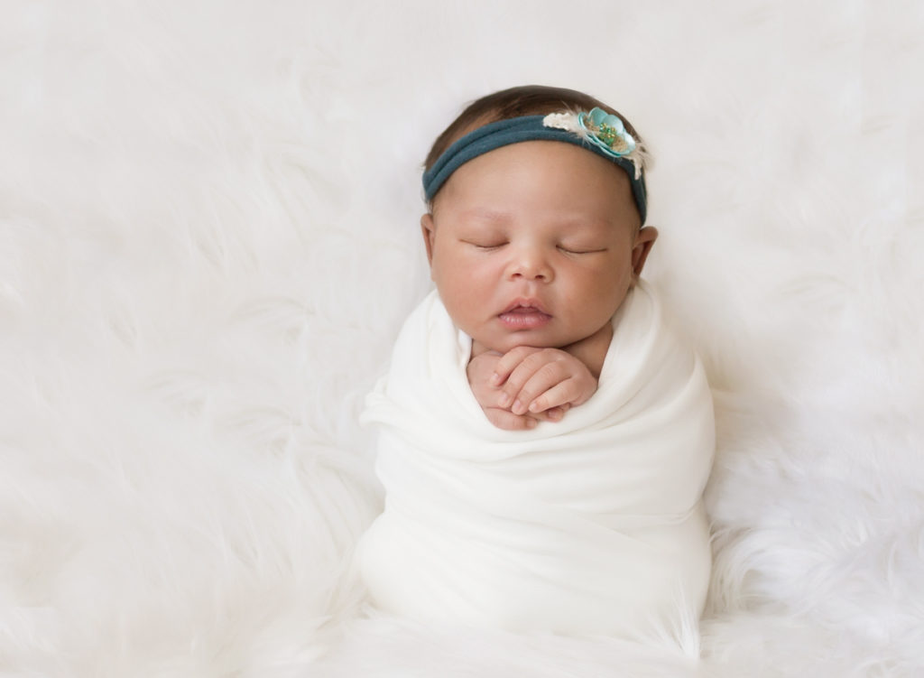 Newborn photo session baby in white potato sack pose with teal headband and flowers