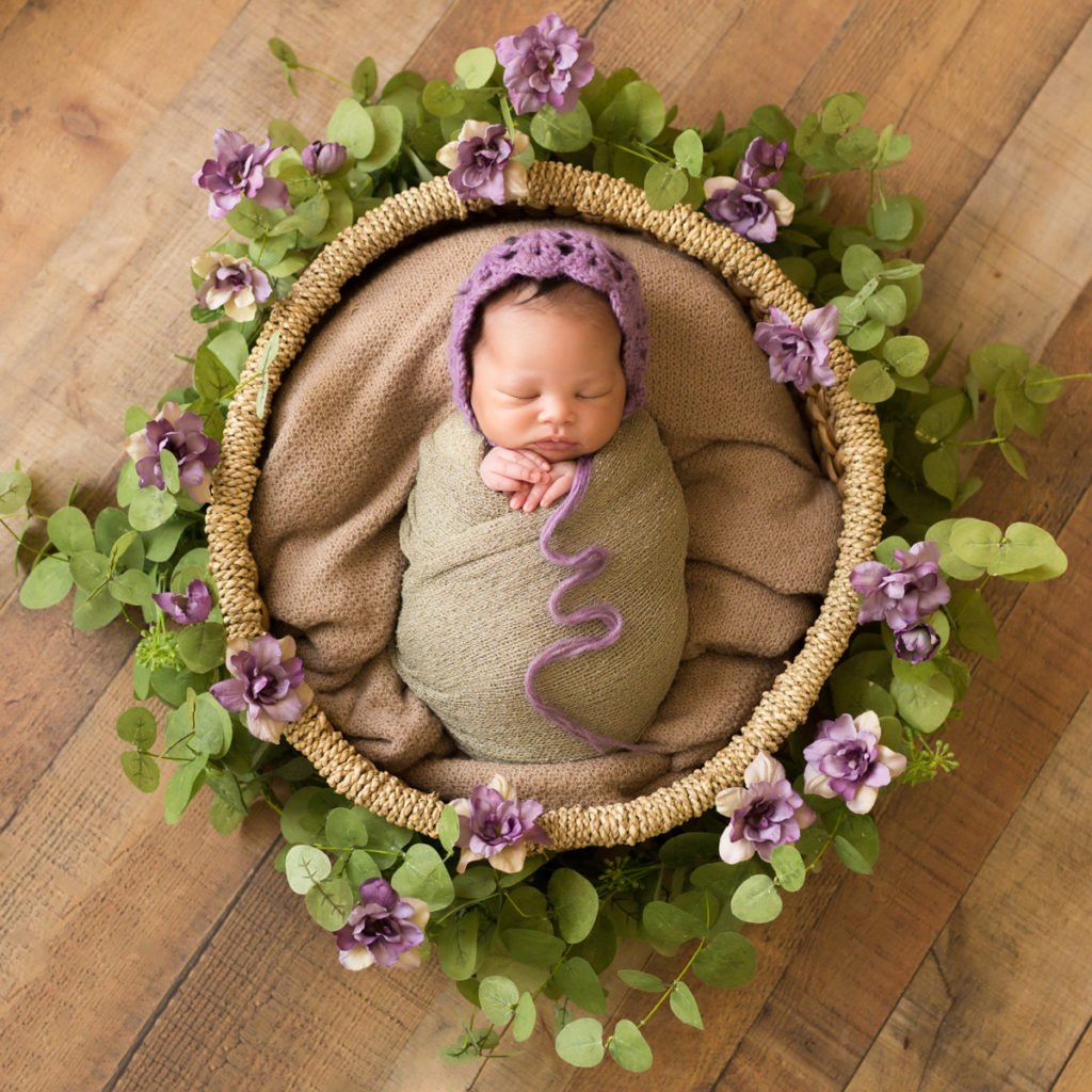 Babygirl with purple bonnet and purple flower basket on wood in Newborn Photosession