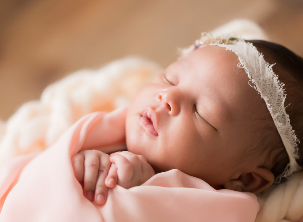 Babygirl face and fingers in peach on chunky knit blanket in Newborn Photosession