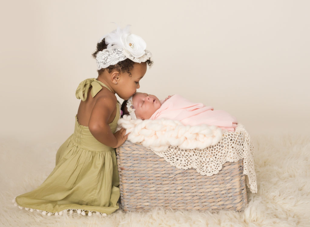Babygirl with happy sister in Newborn Photosession with basket chunky knit blanket and lace