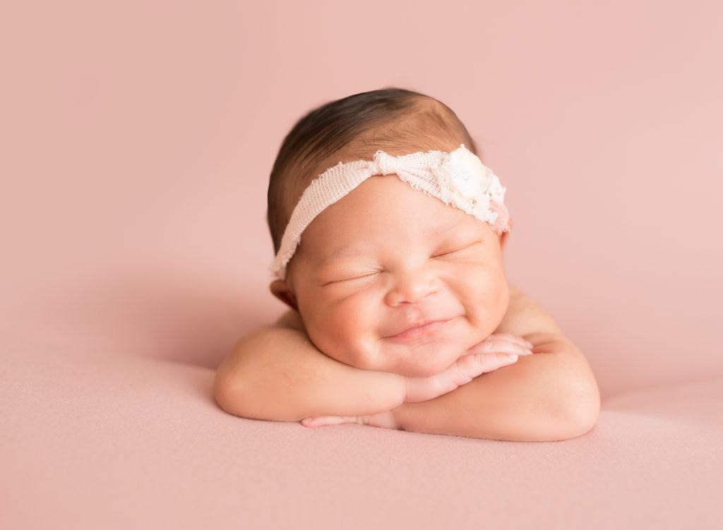 Babygirl grins propped up on arms in Newborn Photosession on Soft Pink Baby Blanket-2