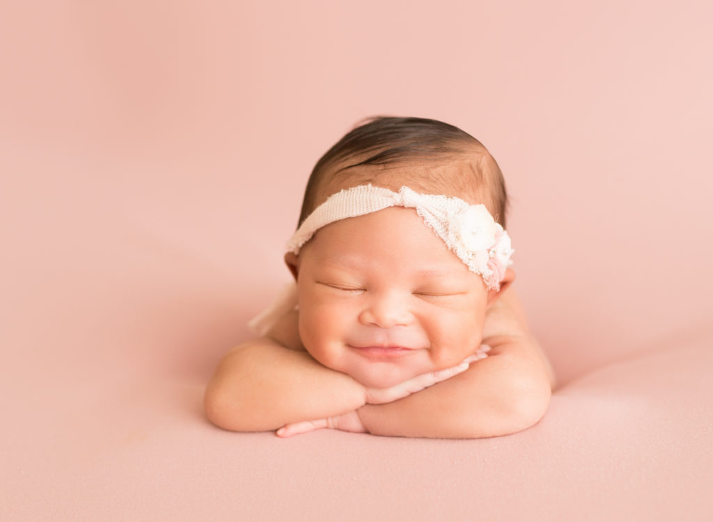 Babygirl grins propped up on arms in Newborn Photosession on Soft Pink Baby Blanket