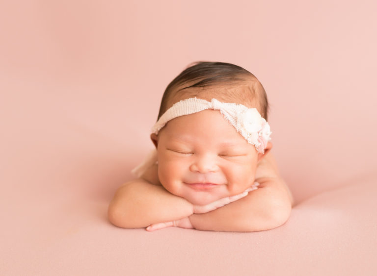 Baby girl grins propped up on arms in Newborn Photosession on Soft Pink Baby Blanket Gainesville Florida