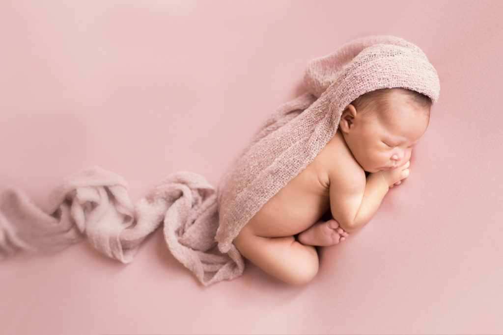 Babygirl posed on belly in Newborn Photosession on Soft Pink Baby Blanket