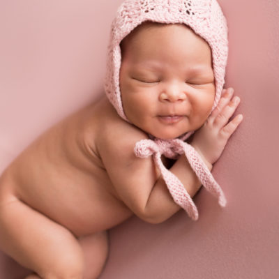 Babygirl grins posed onher side in Newborn Photosession on Soft Pink Baby Blanket