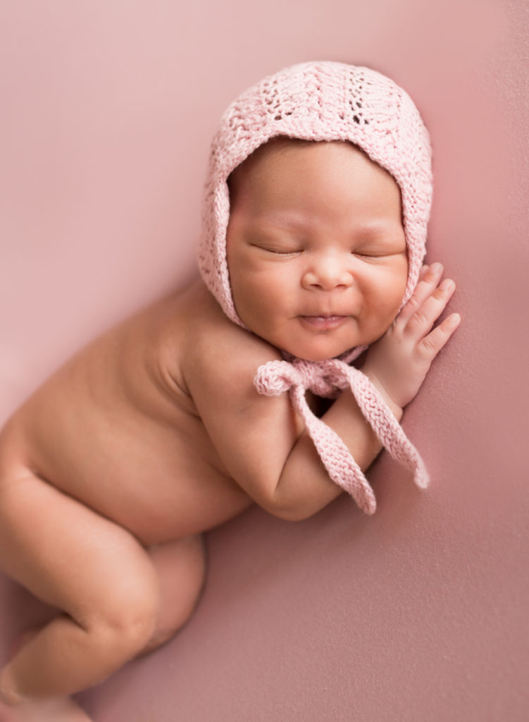 Babygirl grins posed onher side in Newborn Photosession on Soft Pink Baby Blanket