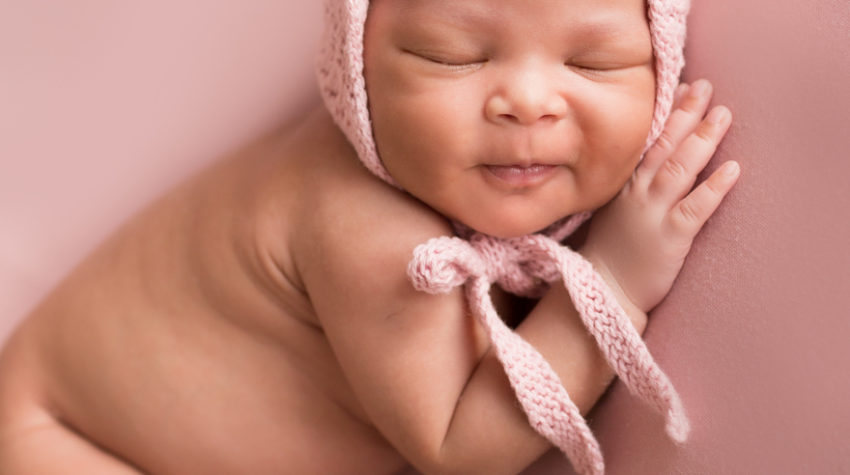 Babygirl grins posed onher side in Newborn Photosession on Soft Pink Baby Blanket