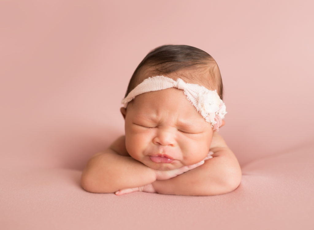 Babygirl funny face propped up on arms in Newborn Photosession on Soft Pink Baby Blanket