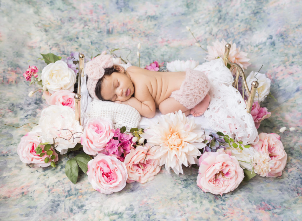 Newborn Girl Haven with full head of hair surrounded with Pink and Peach flowers on Baby Bed with pastel flower background in Gainesville Florida