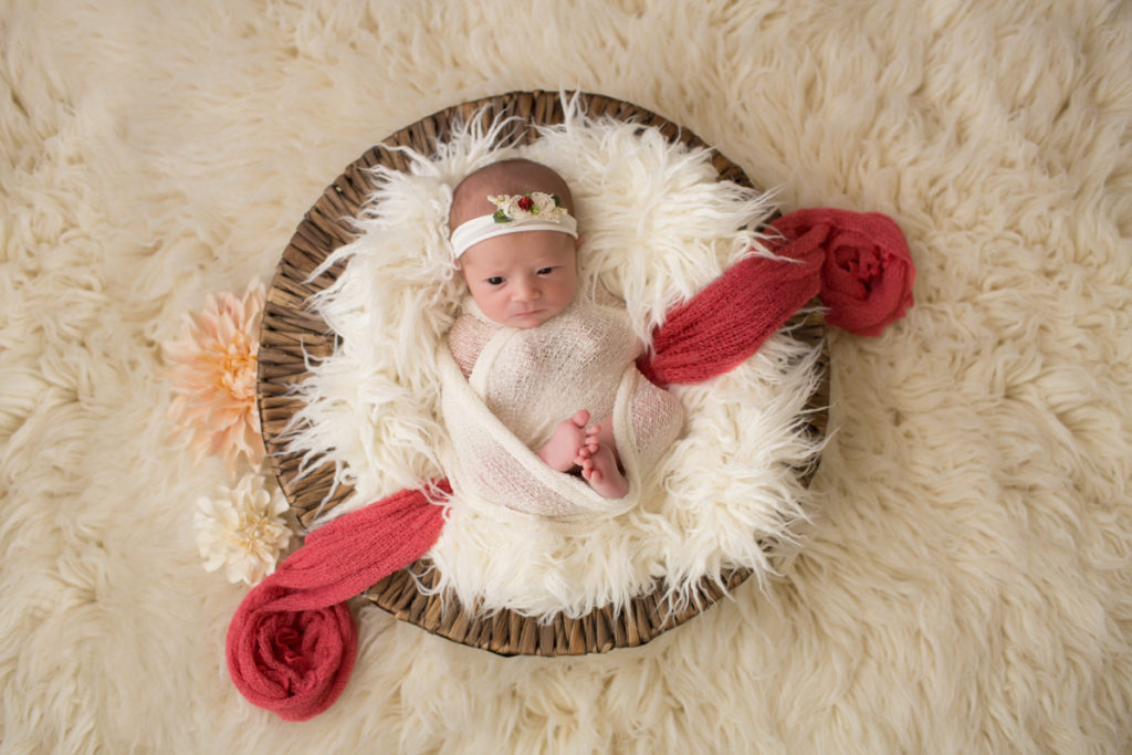 Baby girl Charleigh in round basket with cream fur and peach flowers in Gainesville Florida