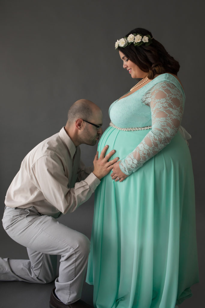 Maternity Photo of Pregnant Adelis in Pale Mint Gown with Dad on bent knee kissing baby bump in Alachua Florida