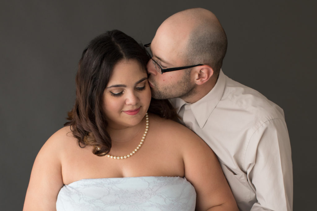 Maternity Indoor Photos of Pregnant Adelis in Blue Lace gown and Pearls getting kiss from husband in Alachua Florida