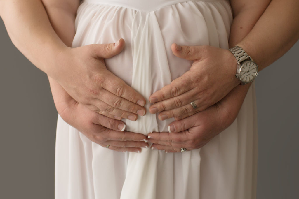 Maternity photo Janet and Nick hands on belly against white gownin Gainesville Florida