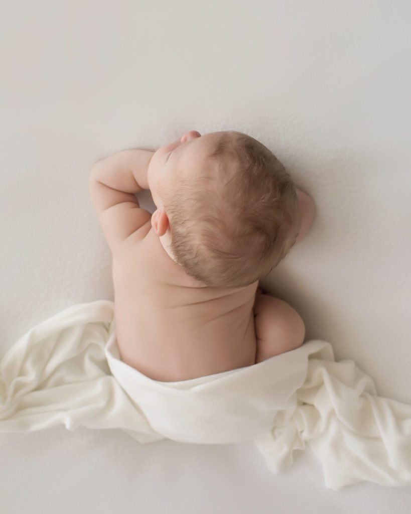 Baby newborn boy in white wrap on white blanket in Gainesville Florida