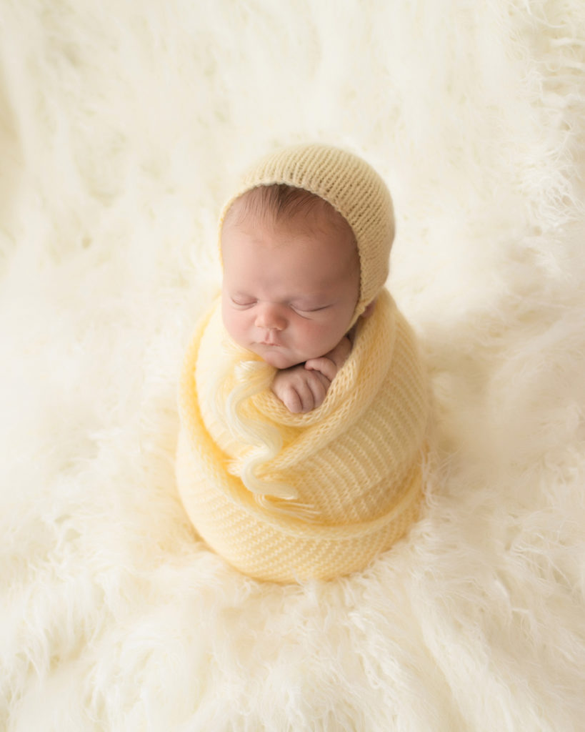 Baby newborn boy wrapped in yellow potato sack and bonnet in Gainesville Florida