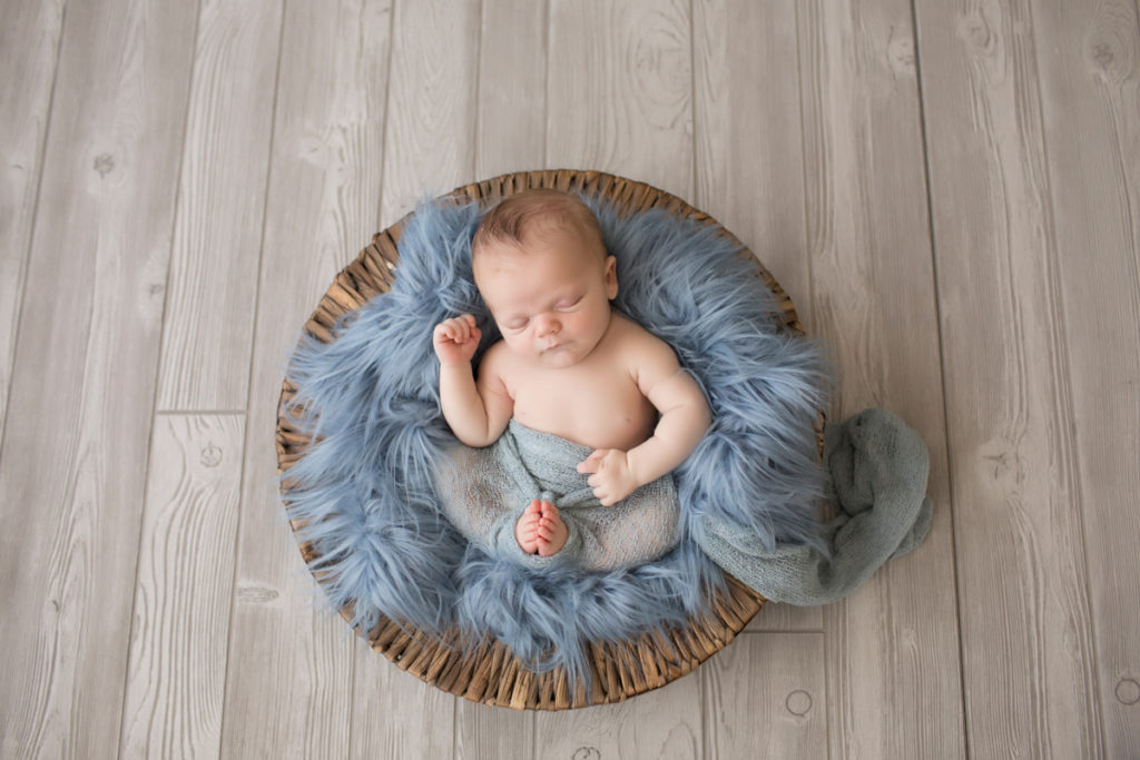 Baby newborn boy in basket with blue fur and wrap in Gainesville Florida