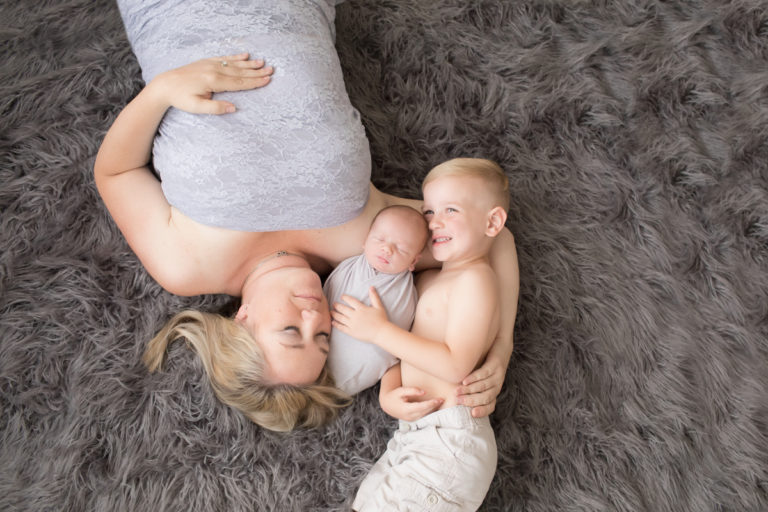 Mom and toddler cuddling newborn baby brother wrapped in grey posed on grey rug in Gainesville Florida