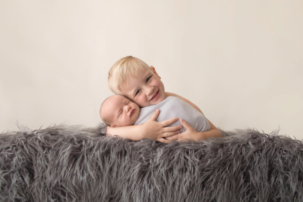 Toddler cuddling baby brother newborn wrapped in grey blanket on grey rug in Gainesville Florida