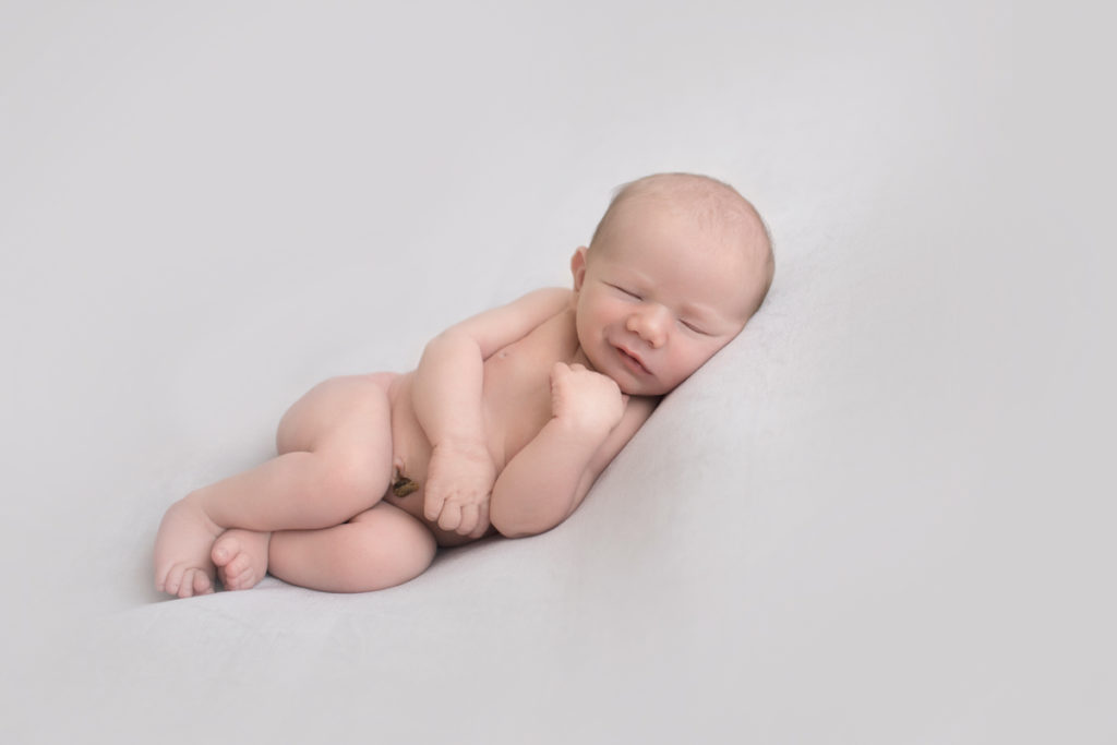 Naked baby newborn boy Chase lying on his side smiling on grey blanket in Gainesville Florida