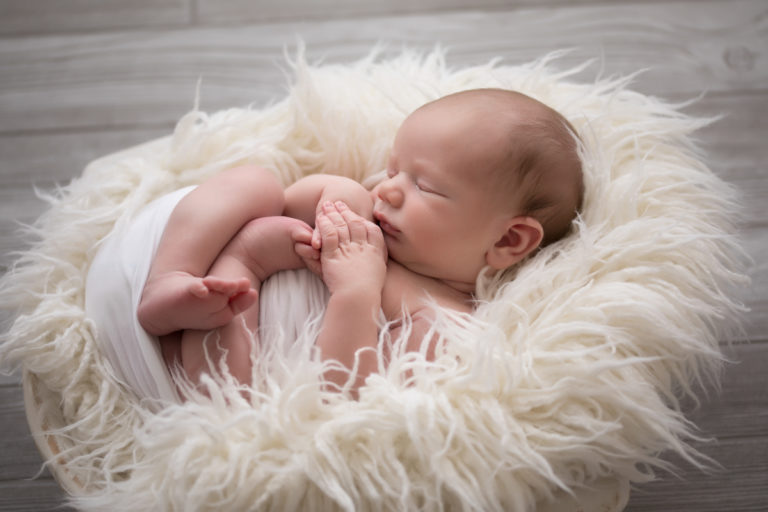 Naked baby newborn boy Chase in basket against grey wood floor with white fluffy basket stuffer in Gainesville Florida