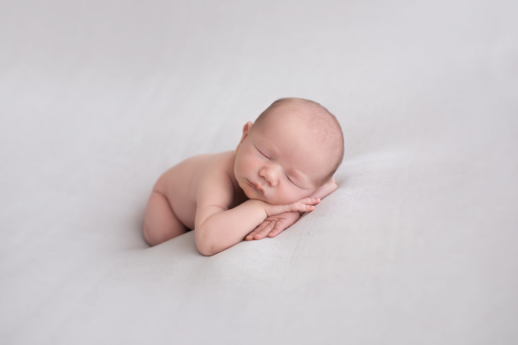 Naked baby newborn boy Chase lying forward resting his cheeks on wrists on top of grey blanket in Gainesville Florida