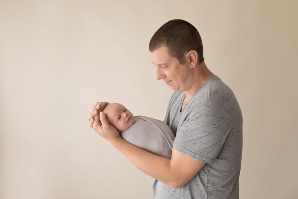 Proud Dad holding his son for first man to man talk both in grey with baby's eyes wide open