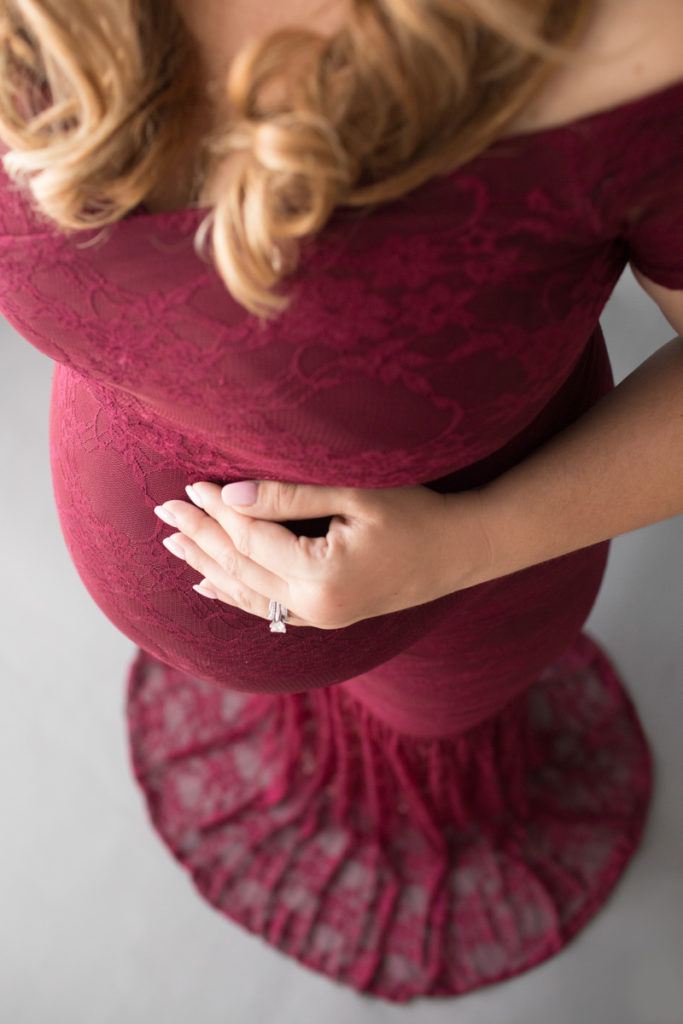 Pregnant mom in burgundy lace mermaid gown viewed from abover her round belly looking down