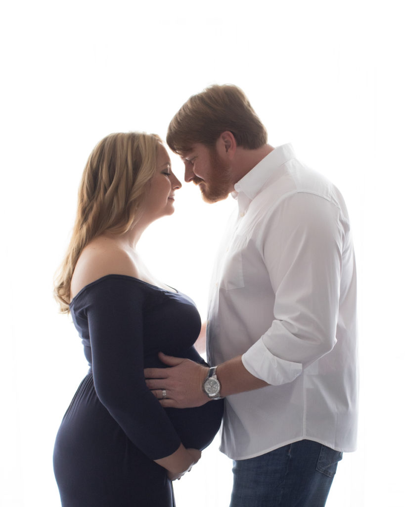 Maternity mom in navy gown with dad in romantic embrace against backlit window