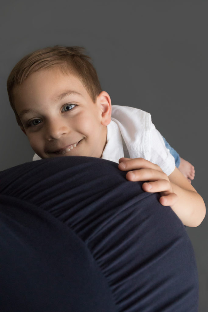 Big brother proudly holds moms pregnant tummy and looks up to his mom with admiration