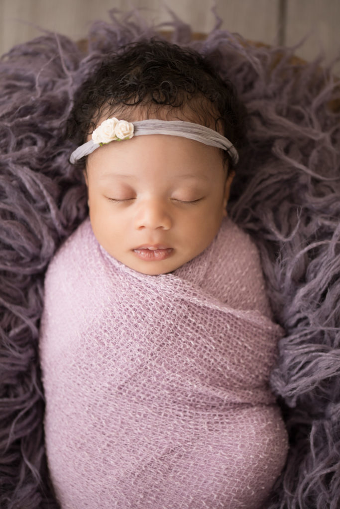 Newborn Girl Ayana close up wrapped in purple shades in purple fur and basket