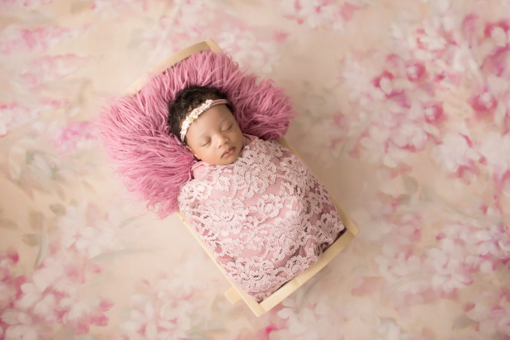 Newborn Girl Ayana wrapped in pink lace shades on pink floral blanket in baby bed
