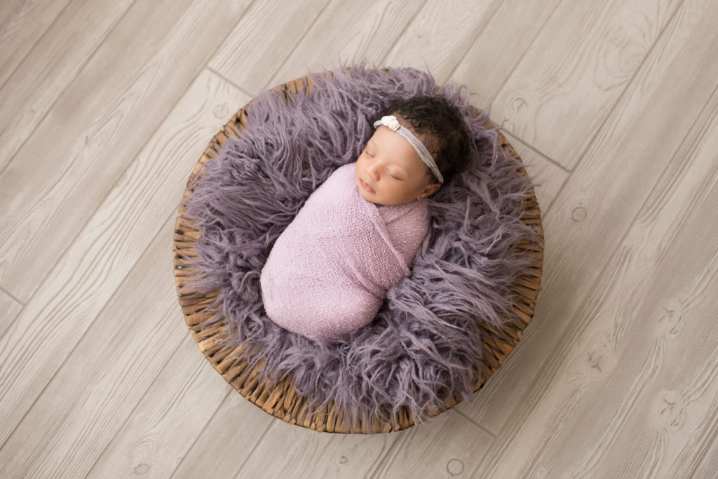 Newborn Girl Ayana wrapped in purple on purple fur in round basket