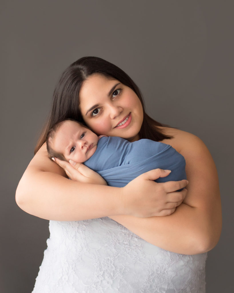 Beautiful new mom cuddling newborn baby boy in blue swaddle with eyes open to camera