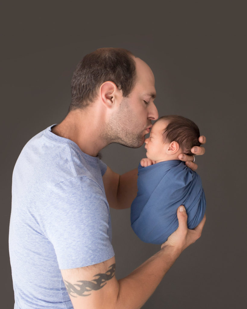 Profile dad with tatoo kissing his newborn baby boy wrapped in blue