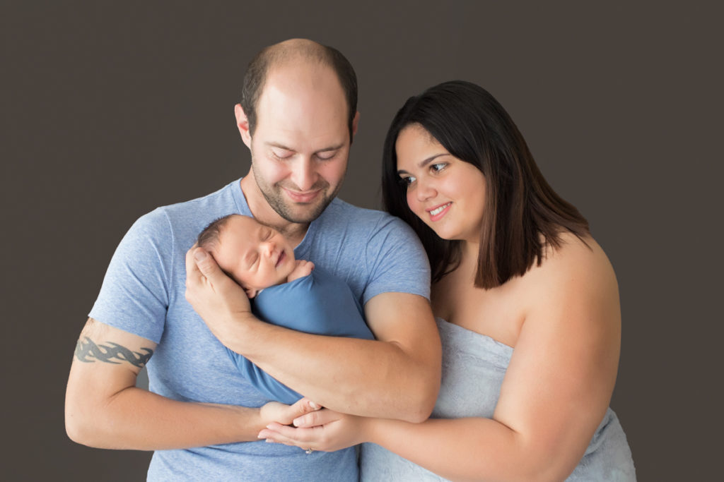 First family portrait mom dad in blues and greys cuddling newborn smiling boy
